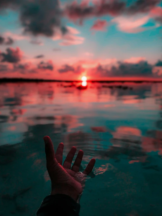 someones hand is held up above the water at sunset
