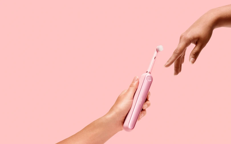a woman is holding a pink toothbrush next to another person's arm