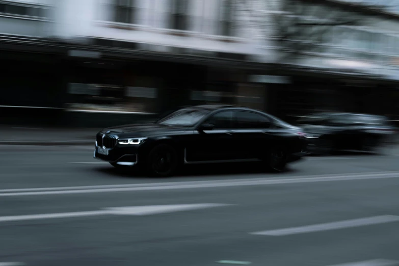 a black car driving down the street with blurry buildings behind it