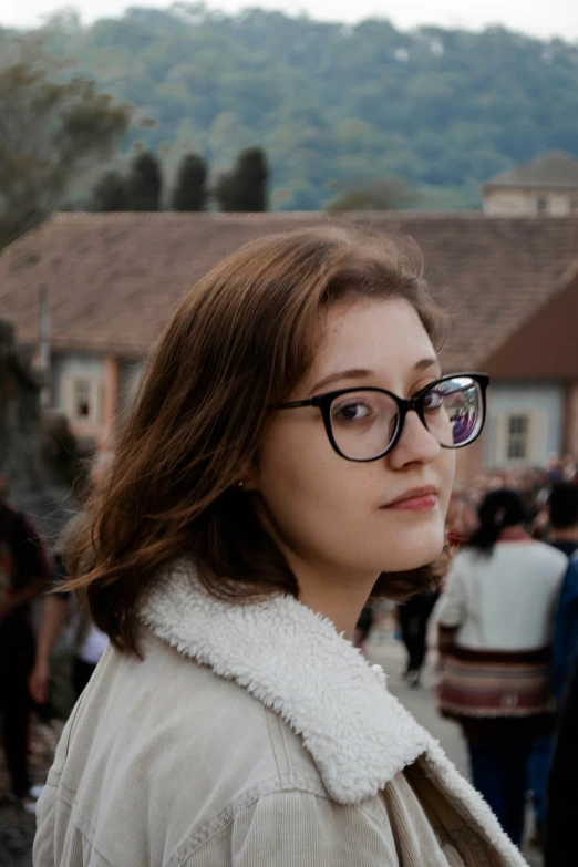 a woman wearing glasses and standing near other people