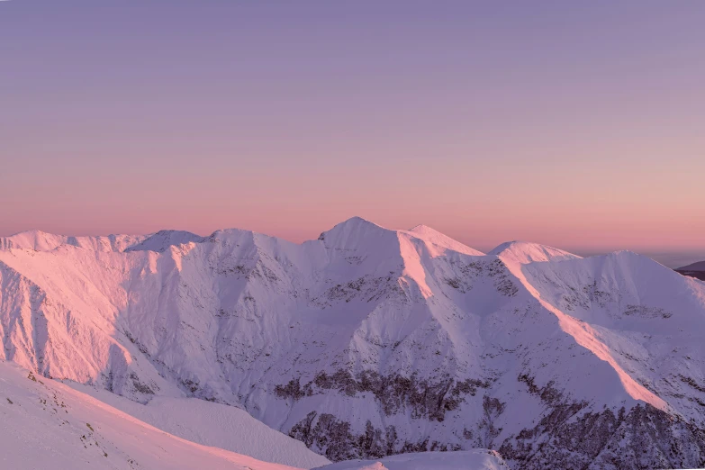 a snow covered mountain range under a pink sky