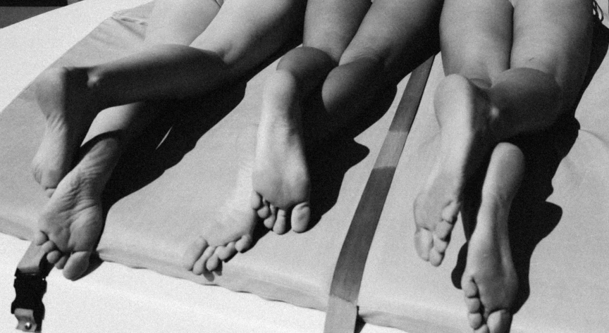 two woman laying down on sheets covered with white sheets