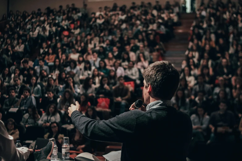 a man in a suit and tie in front of an audience at an auditorium