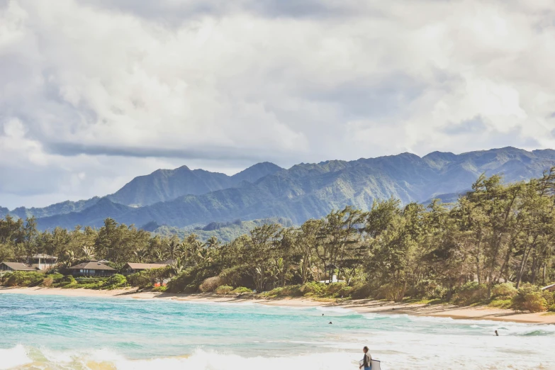 people on the beach with trees and mountains in the background