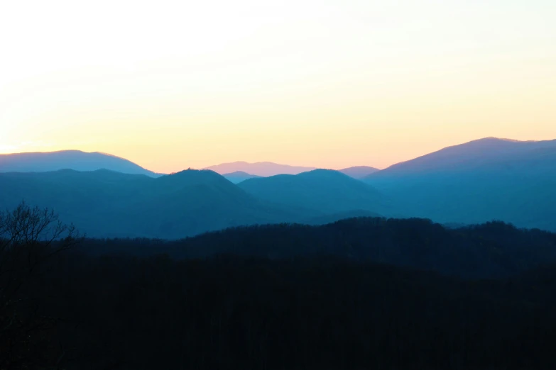 the sun sets over some mountains with no leaves