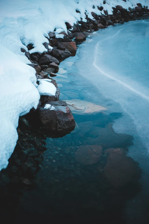 a snowy beach with small rocks and water in the foreground