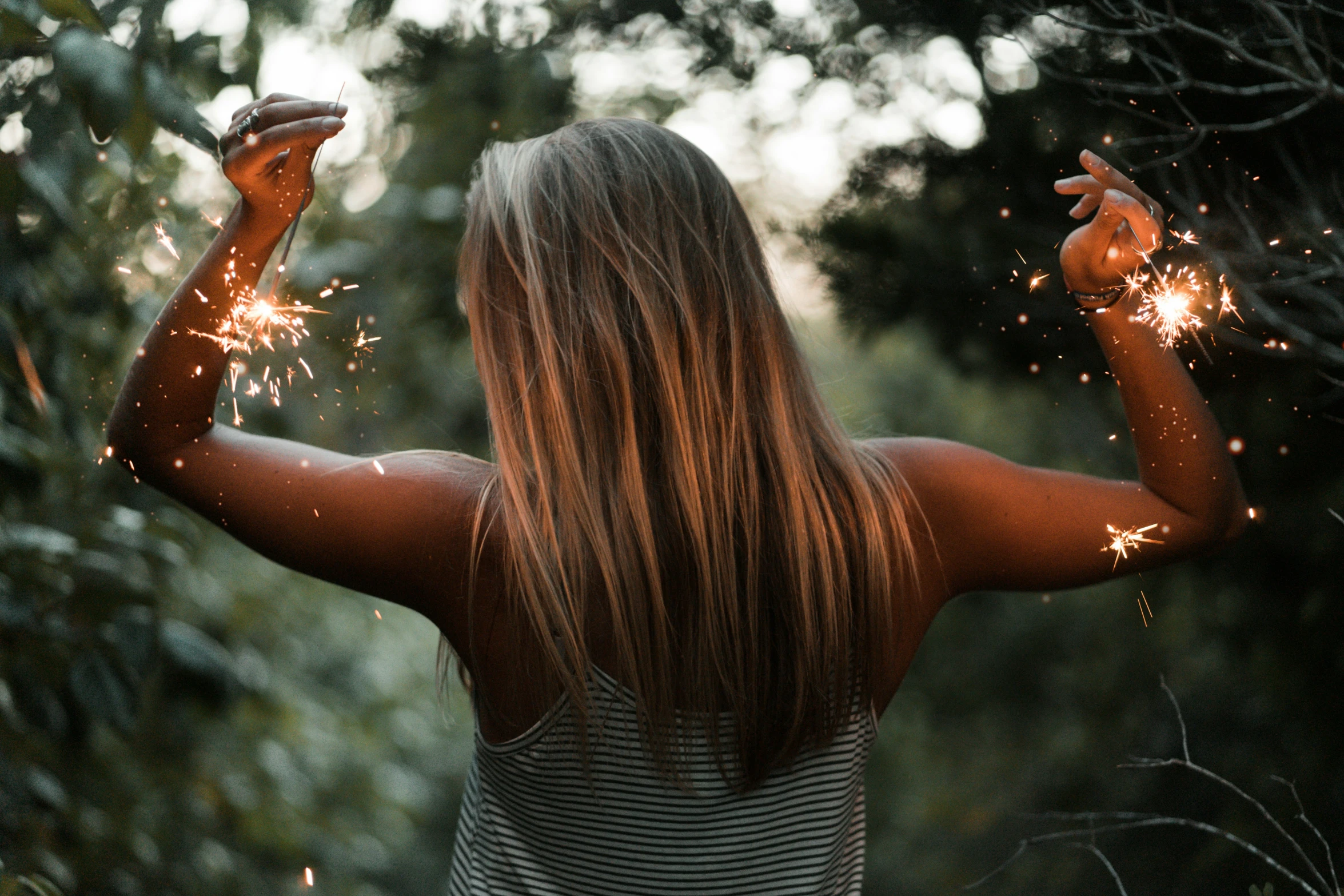 a woman holding firework outside, and holding two hands in the air