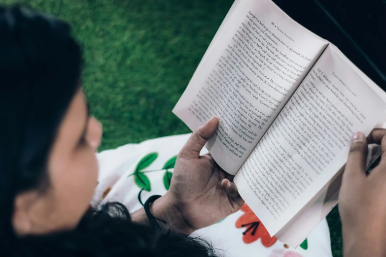 woman laying on grass reading book in outdoor setting