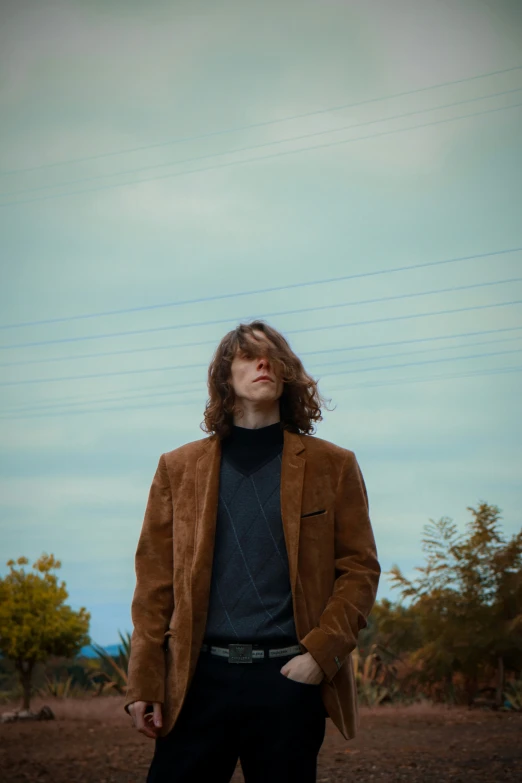 a young man stands on the dirt with his hand in his pockets