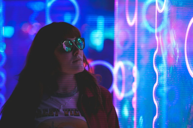 a woman with dark hair and bright sunglasses stands in front of blue and purple light
