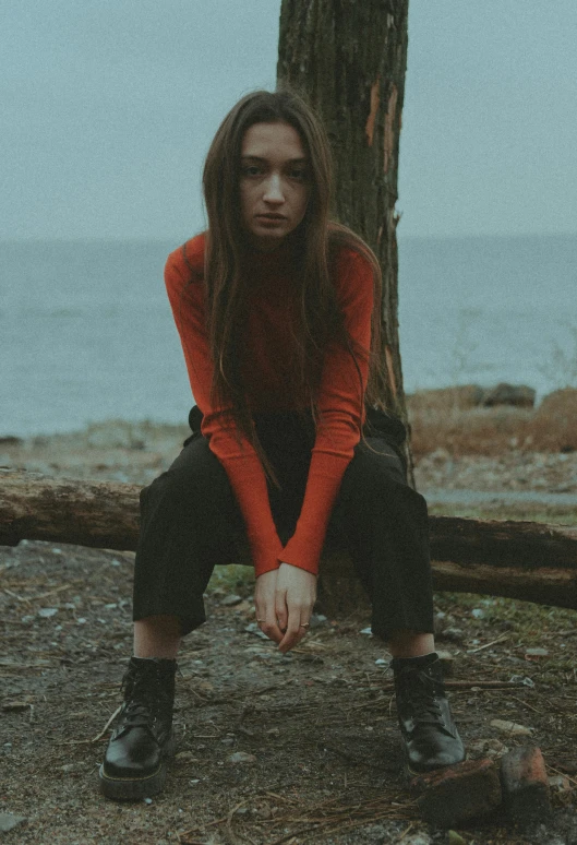 woman in orange shirt leaning against a tree next to the ocean