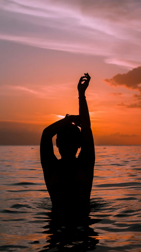 a man in the water at sunset raising his arms up