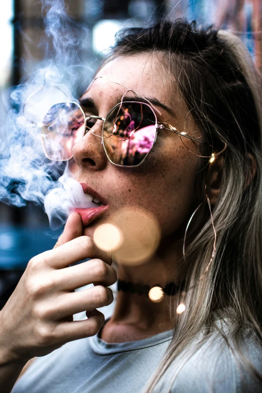 woman with glasses smokes outside near some buildings