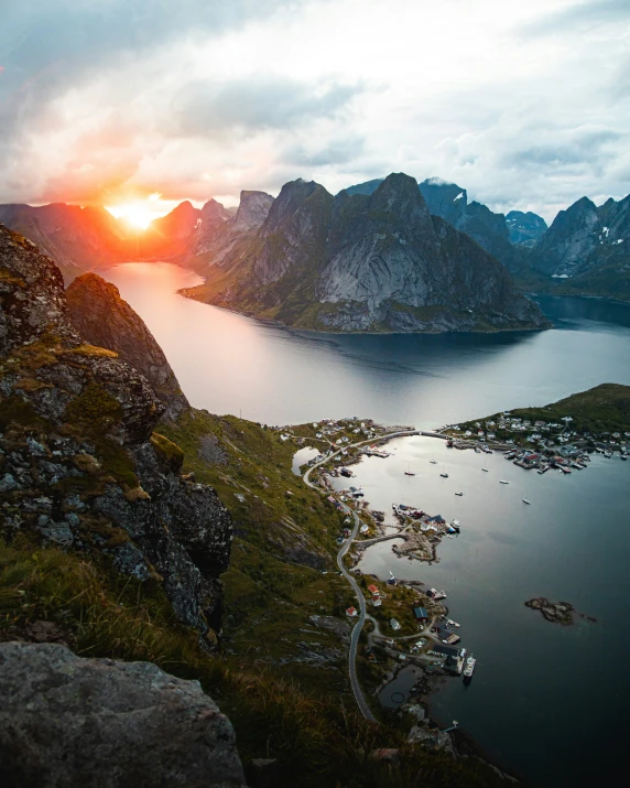 the sun sets over a mountain and small village on water