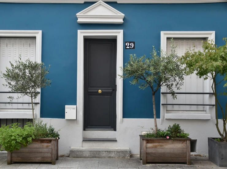 a blue house with white trim and trees planted in front