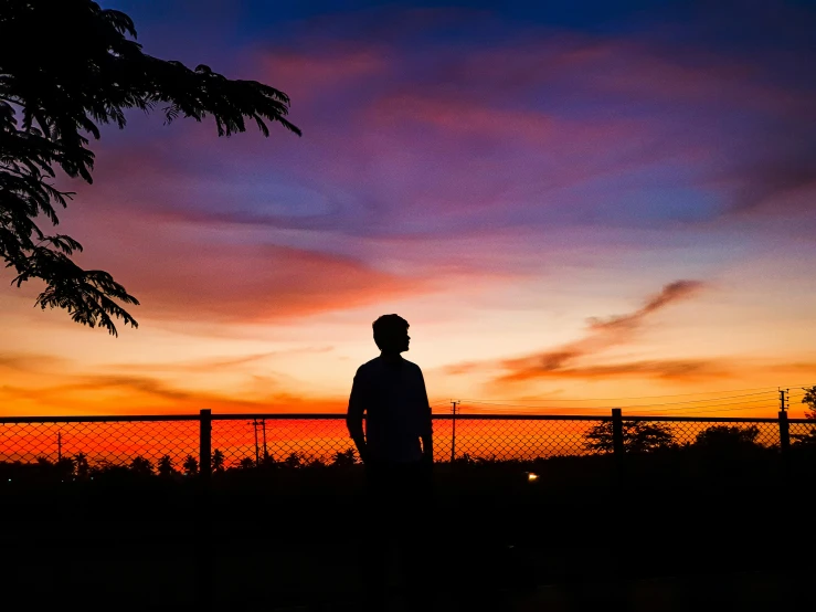 a person standing next to a fence under a sunset