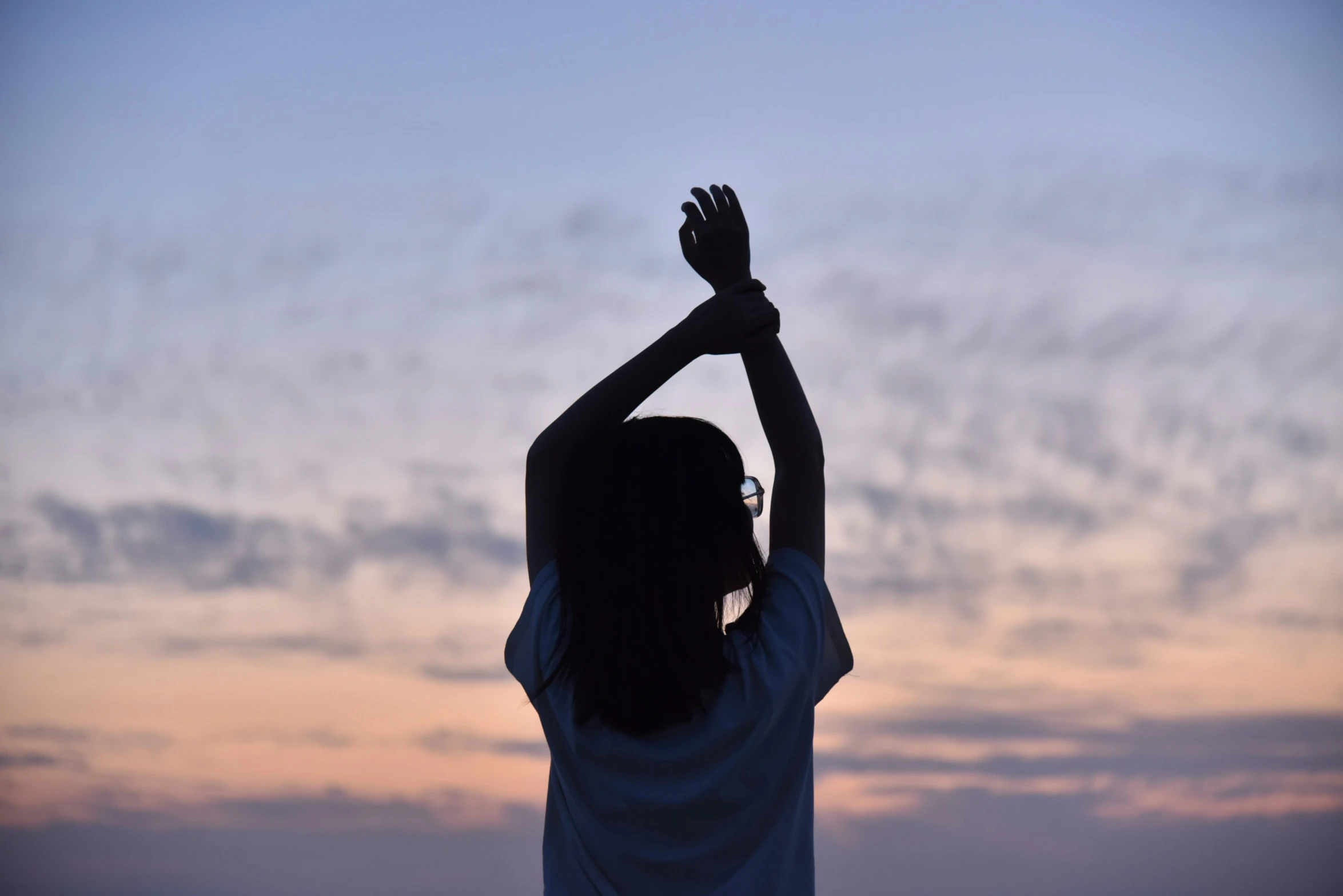 the back end of a girl's hand holding up her hands in the sky