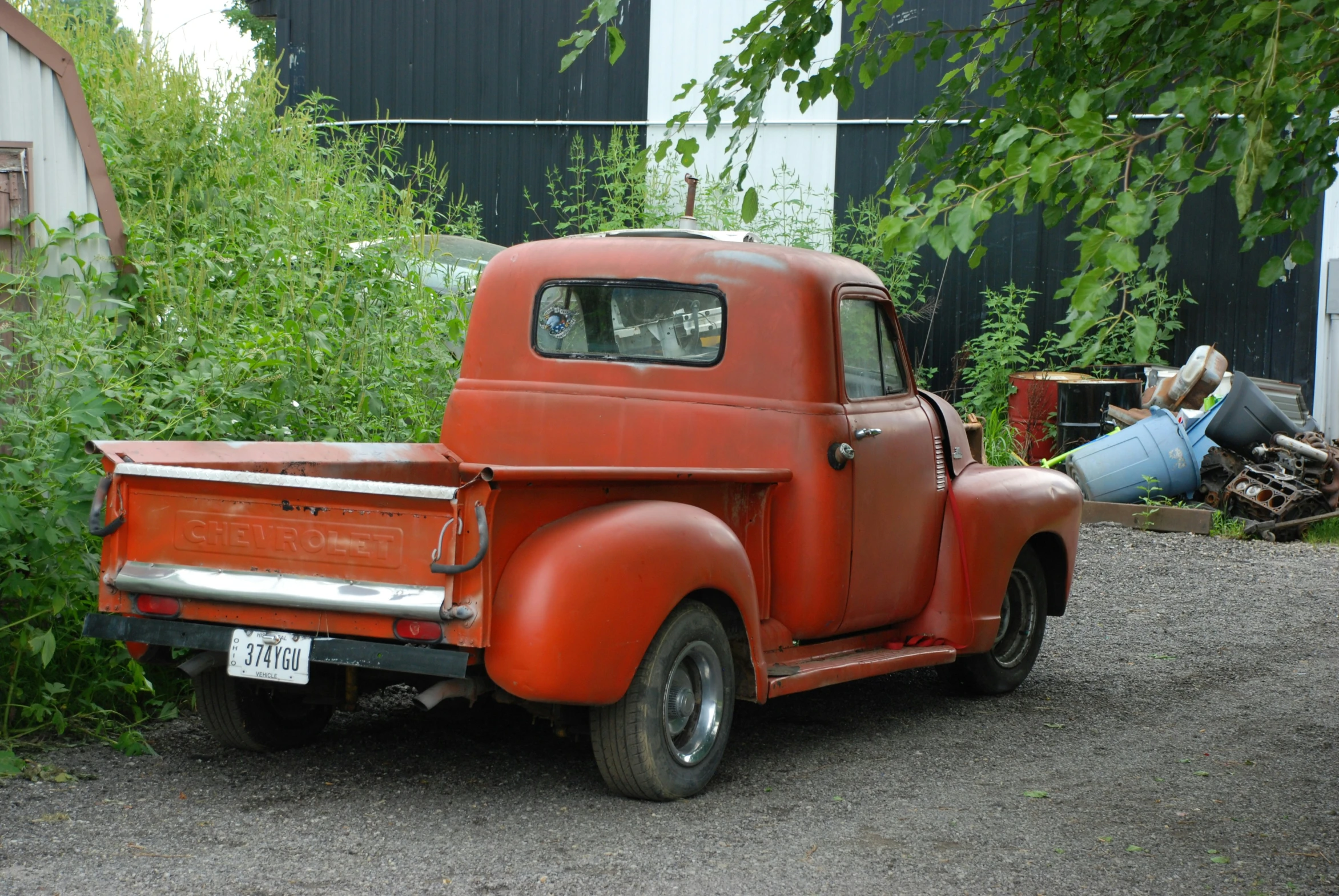 an old truck parked on gravel by bushes