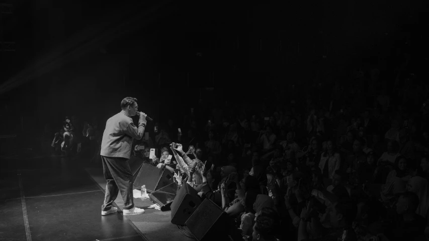 black and white pograph of person on stage while holding microphone