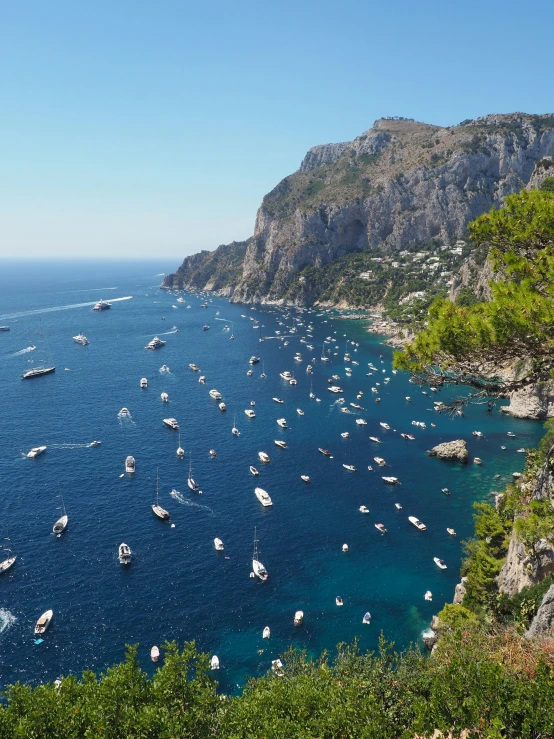 many boats are floating in the water near a cliff