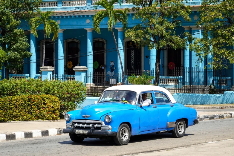 a car drives past a blue building and trees