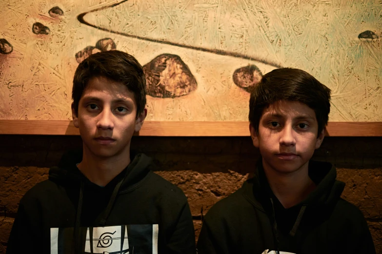 two boys sit next to each other in front of a painting