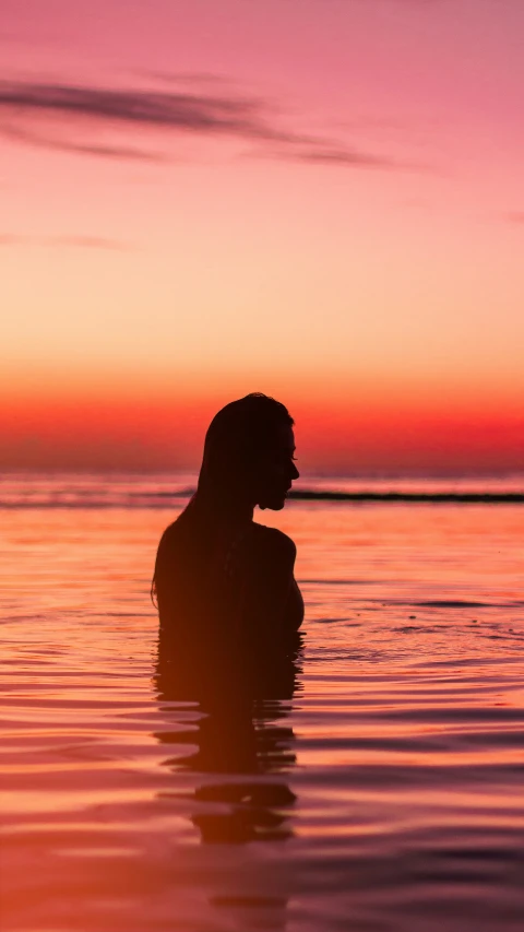 a man standing in the water, silhouetted against an evening sky