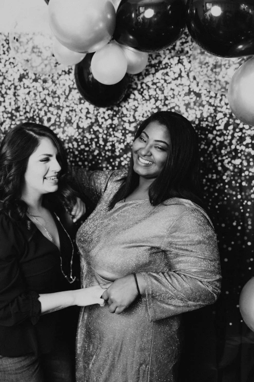 two women standing together by balloons and streamers