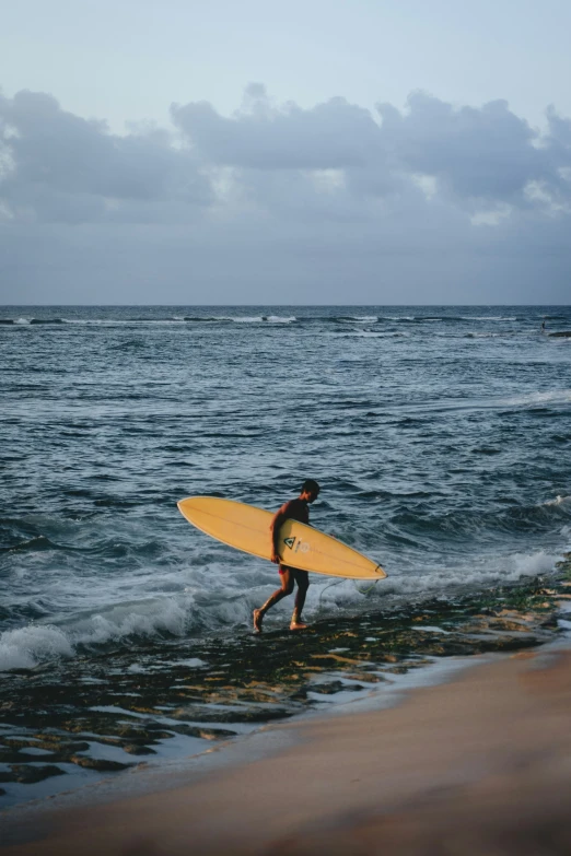 a surfer is heading towards the ocean with a bright yellow surfboard