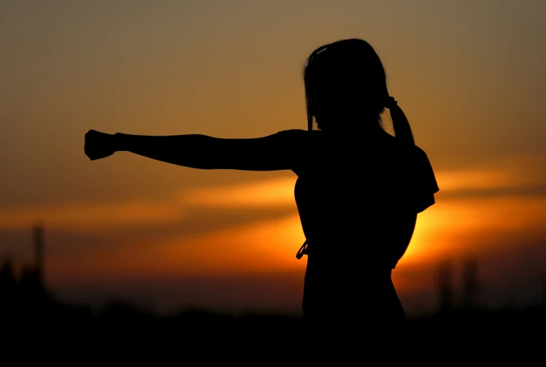 a silhouetted person holding their arms outstretched as the sun sets