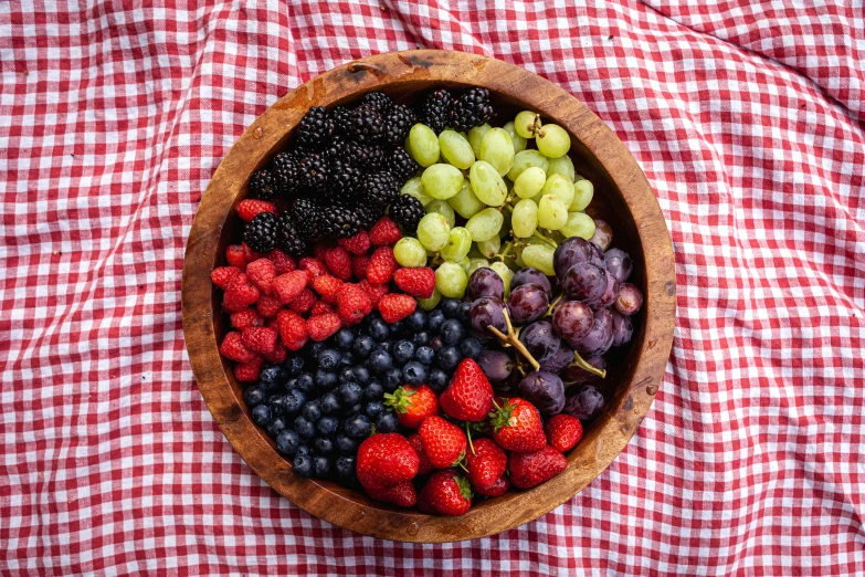 a bowl of berries, gs and strawberries on a red checkered tablecloth