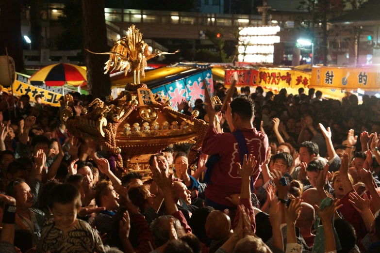 a crowd gathers around a golden statue in a crowded area