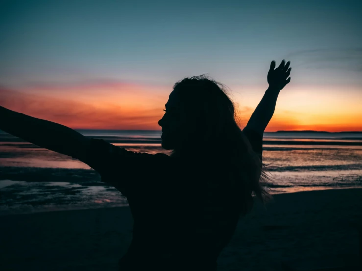 a woman raises her hands up in front of the ocean