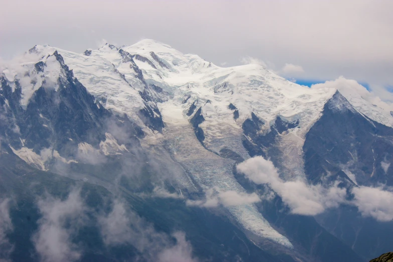 a snowy mountain covered in cloud next to a forest