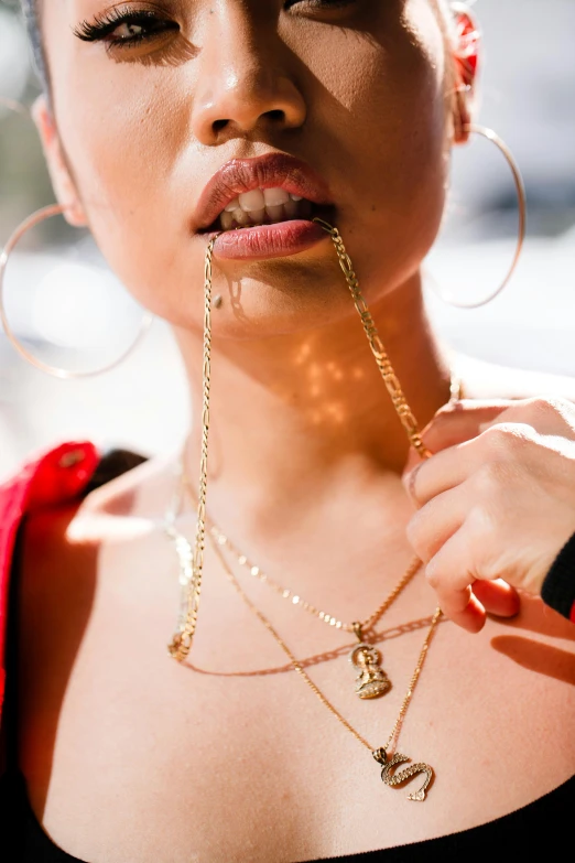 a close up view of an asian woman wearing large hoop earrings and holding a chain in her mouth