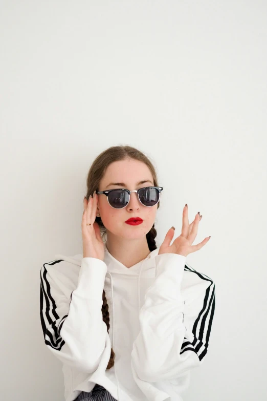 a woman wearing sunglasses and posing in front of a white wall