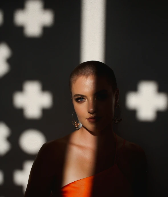 a woman wearing earrings and an orange dress standing in the shadow