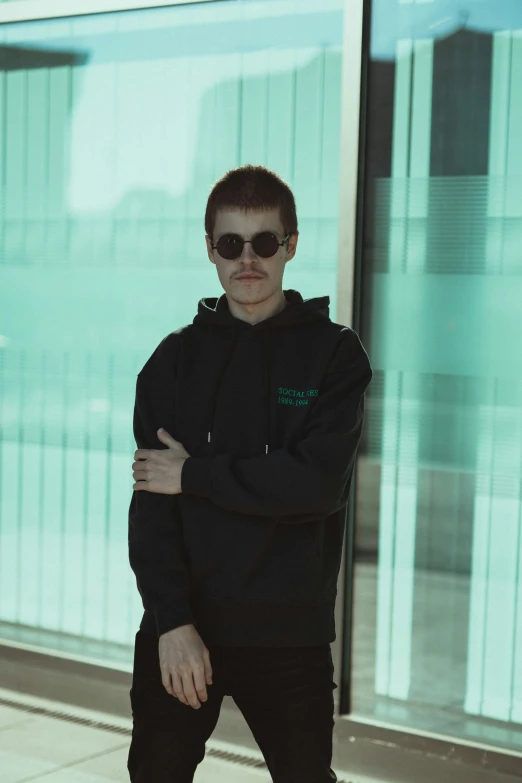 a young man wearing sunglasses walking near large window