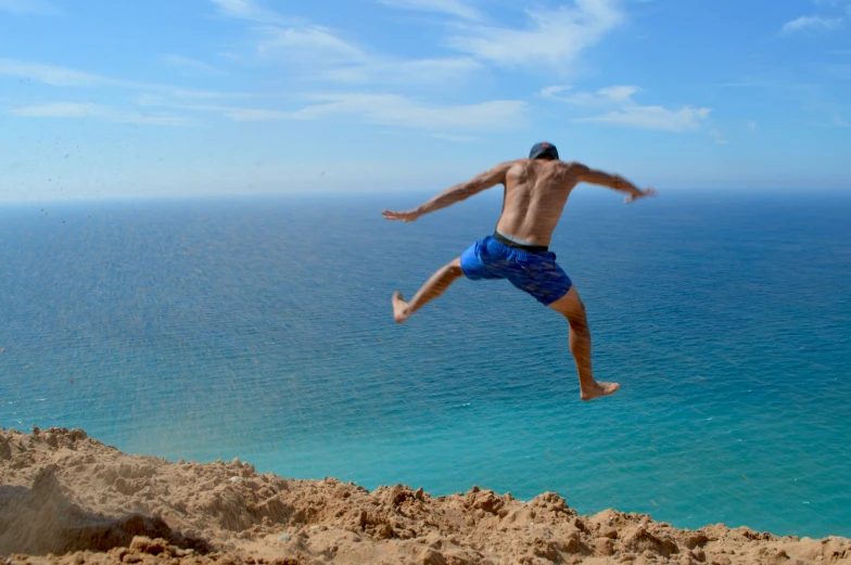 a shirtless man wearing blue shorts jumps into the air