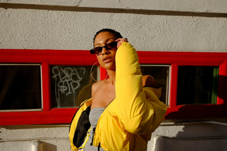 a woman wearing a yellow puffer jacket leaning up against a wall