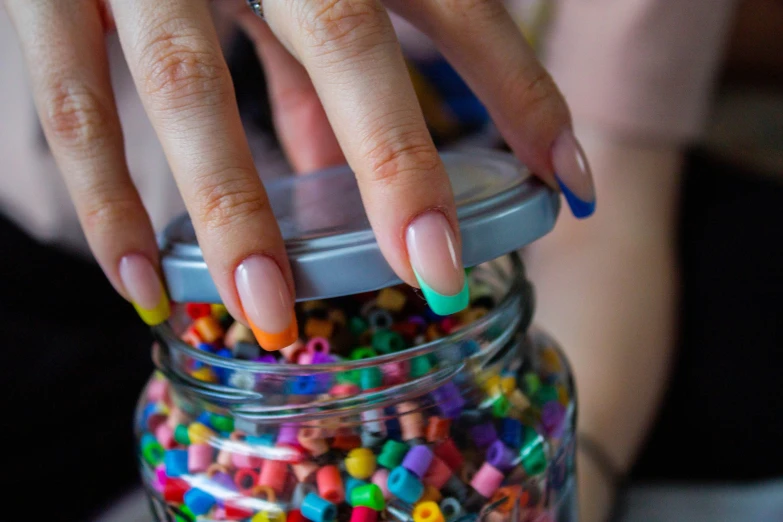 someone holding their hand over a jar full of colored beads