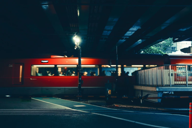 a red train traveling under an overpass in the night