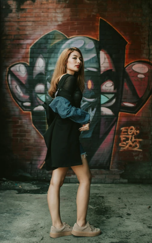 a girl standing in front of graffiti holding a purse