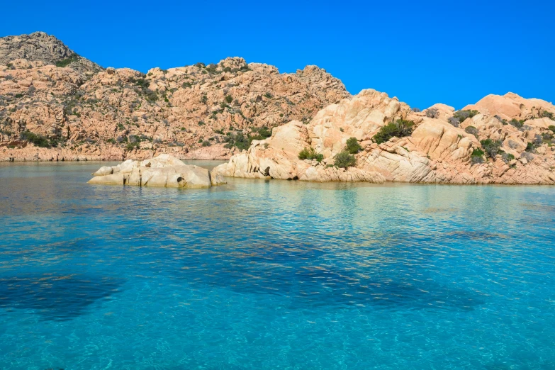 clear blue water and mountains in front of a rock wall