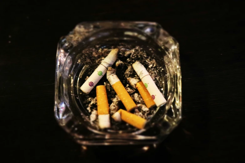 a glass ashpot full of cigarettes on top of a wooden table