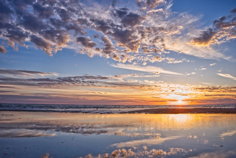 a beach with a boat in the water and clouds reflected