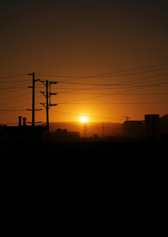 there is a sunset seen with wires attached to the telephone pole