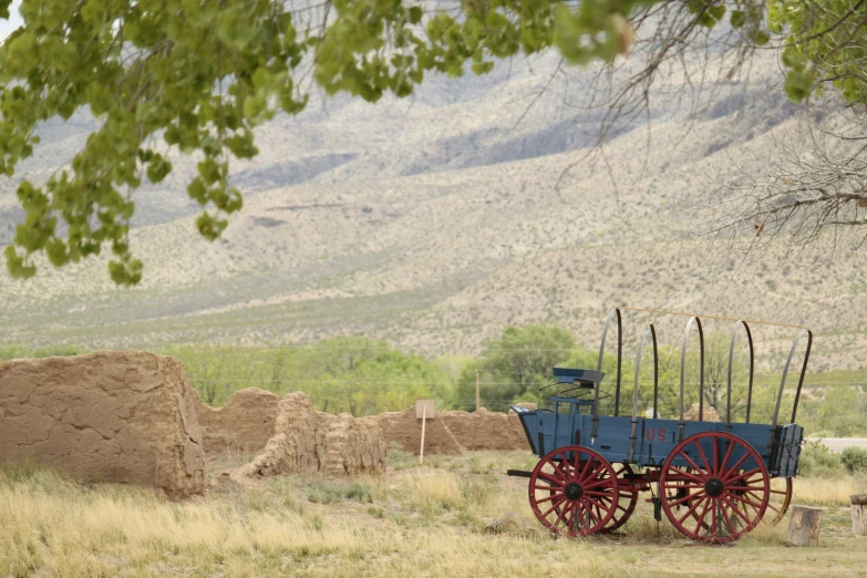 a blue carriage with four wheels sits under a tree