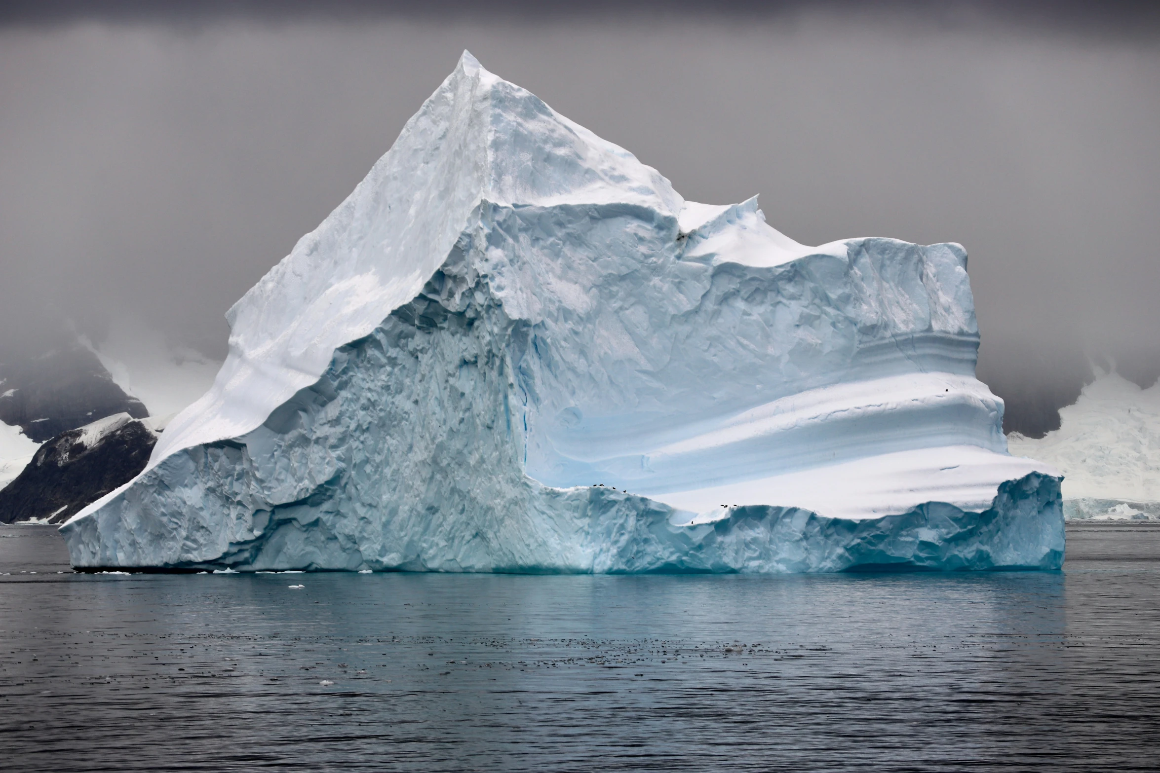 an iceberg is floating in the ocean in cloudy weather