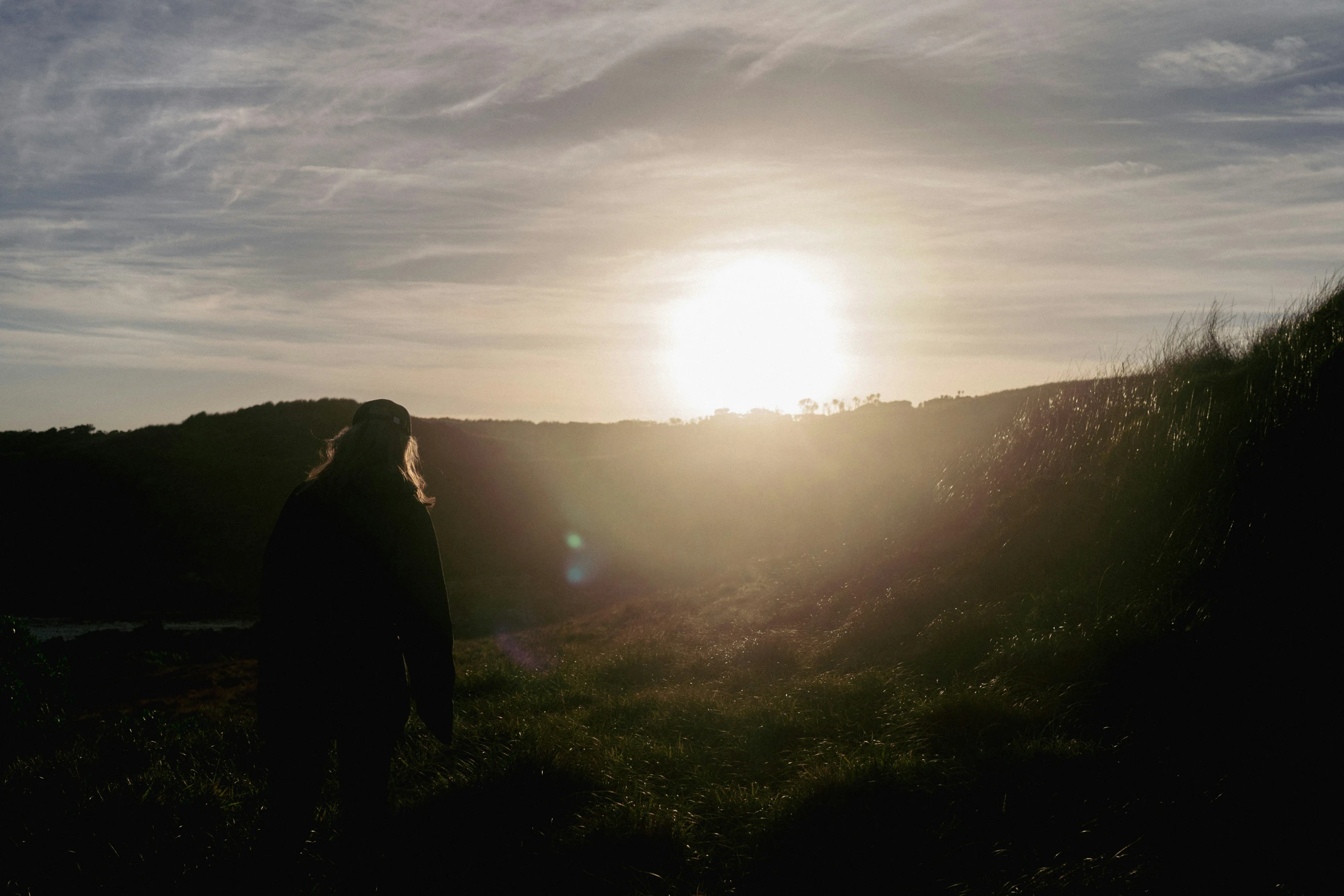 the sun is shining behind a grassy hill side